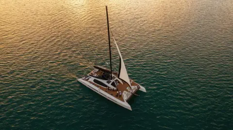 Sailing catamaran on golden water at sunset, from above