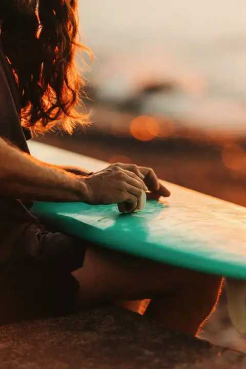 Hands waxing a surfboard in warm evening light